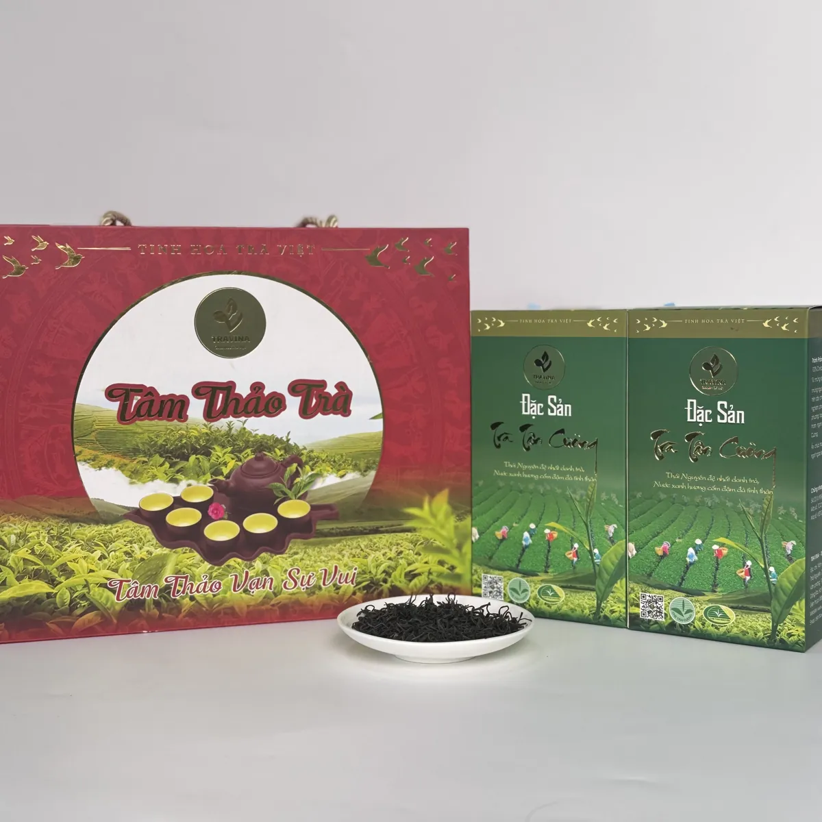 Hộp quà Tâm Thảo Trà bên hai hộp trà xanh và đĩa trà khô – TRAVINA HTX Tâm Trà Việt