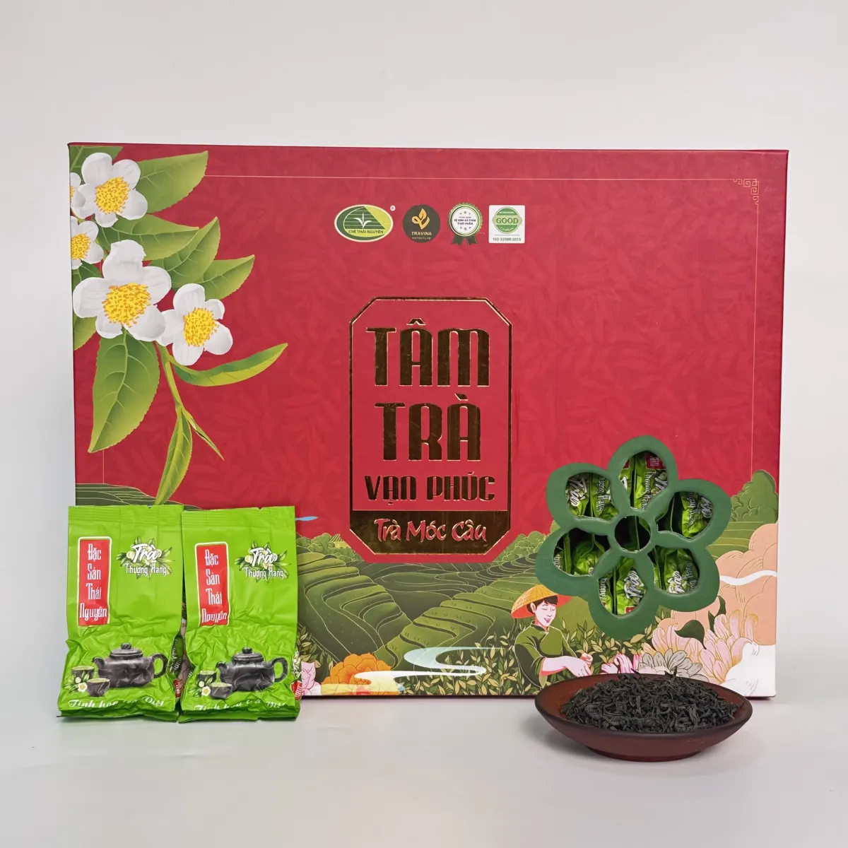 Hộp quà Tâm Trà Vạn Phúc (Trà Móc Câu) bên hai gói trà nhỏ và đĩa trà khô – TRAVINA HTX Tâm Trà Việt