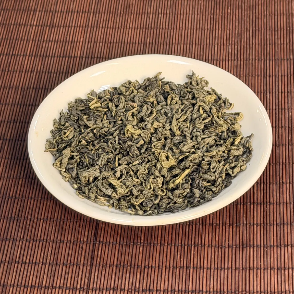 Trà xanh khô cánh xoăn nhỏ màu xanh vàng trên đĩa sứ trắng, dạng trà nền nõn để ướp hoa nhài