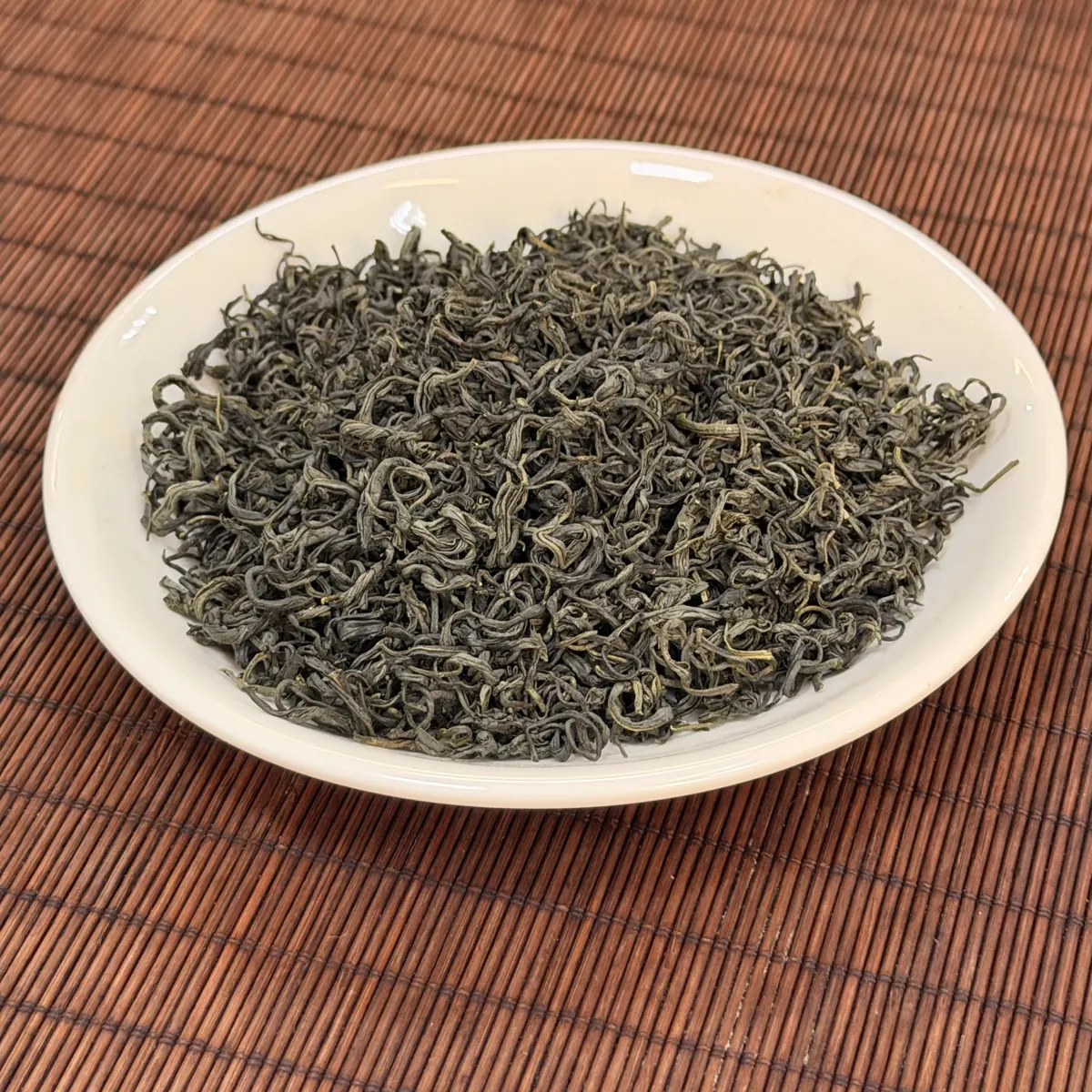 Trà xanh khô sợi dài xoăn trên đĩa sứ trắng, kiểm tra cánh trà trước khi pha trà nhài cho quán