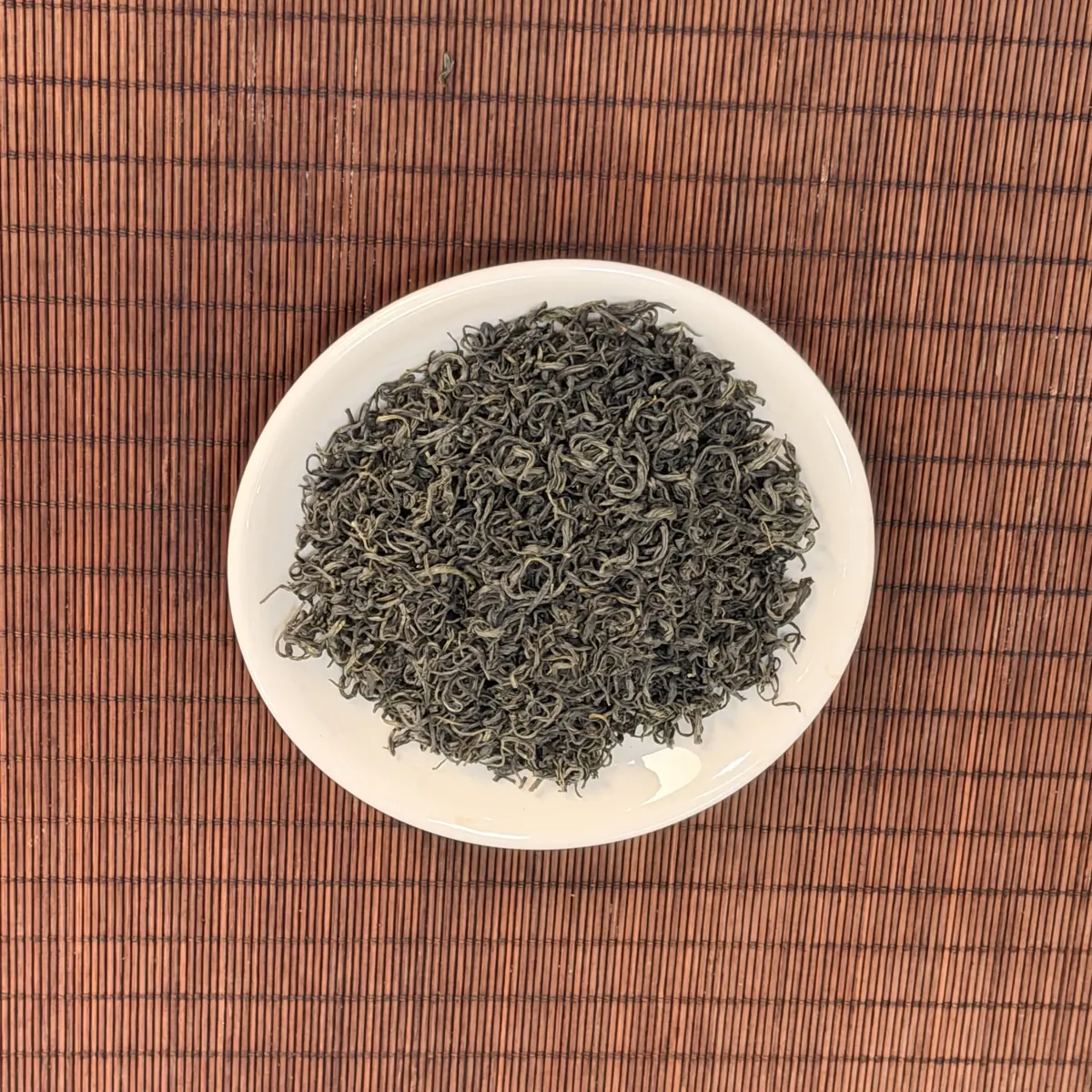 Đĩa trà xanh khô sợi nhỏ xoăn chụp từ trên xuống trên mành tre, nghiệm thu lô trà cho quán